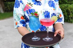 a woman holding a tray with two cocktails on it at Deva Beach Resort Samui in Choeng Mon Beach