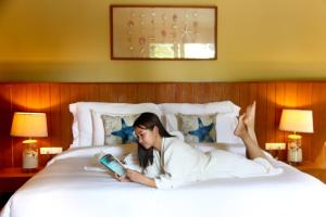 a woman laying on a bed reading a book at Deva Beach Resort Samui in Choeng Mon Beach