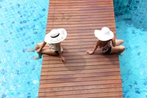two children wearing hats sitting on a wooden walkway in a pool at Deva Beach Resort Samui in Choeng Mon Beach