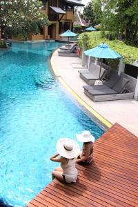 two women sitting next to a swimming pool at Deva Beach Resort Samui in Choeng Mon Beach