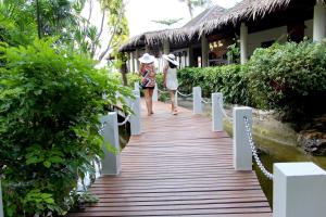 two women walking down a wooden walkway in front of a building at Deva Beach Resort Samui in Choeng Mon Beach
