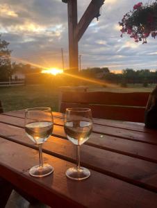 two wine glasses sitting on a wooden table with the sunset at Tulipános Vendégház in Igrici