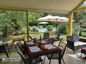 einen Tisch mit Stühlen und einem Sonnenschirm auf einer Terrasse in der Unterkunft Haut de villa : véranda, terrasse, vue piscine in Thiviers