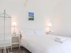 a white bedroom with a white bed and two lamps at Pollards Cottage in Forrabury