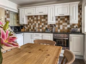 a kitchen with white cabinets and a wooden table at Beech Cottage - Uk44731 in Hartington