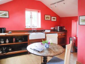 uma cozinha com paredes vermelhas, uma mesa e um lavatório em The Byre em West Stour
