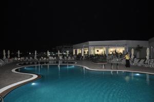 a woman standing next to a swimming pool at night at Royal Bay Suites in Kefalos