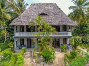 a house with a thatched roof and palm trees at Michamvi Sunset Bay in Michamvi