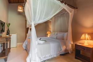 1 dormitorio con cama con dosel y cortinas blancas en Pousada Recanto do Sol, en Trancoso
