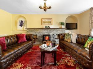 a living room with brown leather couches and a fireplace at Manor Farm in Coffinswell