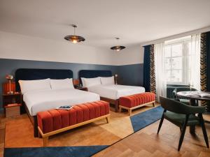 a bedroom with two beds and a chair and a table at The Hoxton, Lloyd Amsterdam in Amsterdam