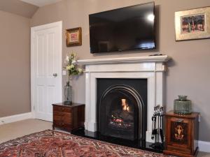 een woonkamer met een open haard en een televisie erboven bij Gardeners Cottage in Montrose