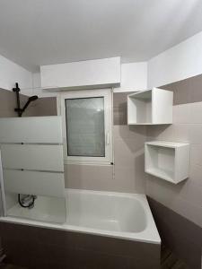 ein weißes Bad mit einer Badewanne und einem Fenster in der Unterkunft Studio lumineux en bord de mer in Pléneuf-Val-André