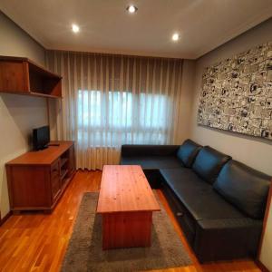 sala de estar con sofá negro y mesa de madera en Apartamento Coqueto 10min centro en Oviedo