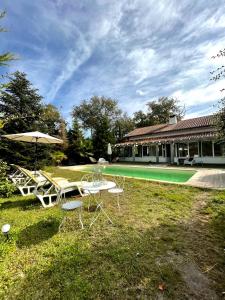 uma mesa e cadeiras com um guarda-sol ao lado de uma piscina em Gîte familial en pleine nature- Domaine Temali em Labouheyre