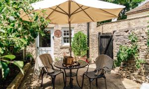 een tafel en stoelen met een parasol op een patio bij Delightful Cotswold Cottage for two, Log Burner, Garden & Dog Friendly in Northleach