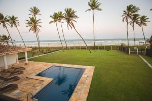 einen Hinterhof mit einem Pool und einer Liegewiese mit Palmen in der Unterkunft Maravilhosa casa em Vilas do Atlantico frente ao mar in Lauro de Freitas