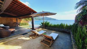 a patio with chairs and an umbrella and the ocean at Casa da Ilha in Praia de Araçatiba