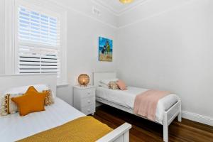 a white bedroom with two beds and a window at EDW19 - Stylish 2-Bed, 2-Bath Townhose in Drummoyne in Sydney