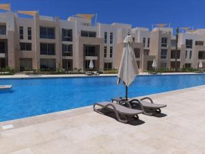 ein Sonnenschirm und ein Liegestuhl neben einem Swimmingpool in der Unterkunft Warm 1BR with at Mangroovy, El-Gouna M1-7B in Hurghada