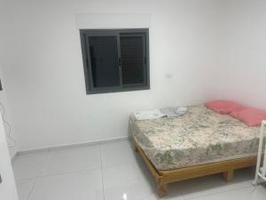 a small bed in a white room with a window at the village in Yeroẖam