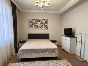 Schlafzimmer mit einem Bett, einem TV und einem Kronleuchter in der Unterkunft Aikol in Bischkek
