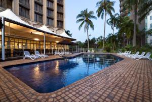 a swimming pool with white chairs and a building at Hilton Garden Inn Darwin in Darwin