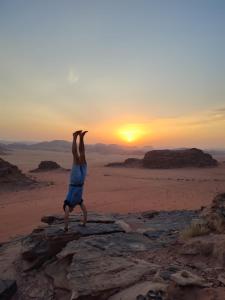 een man die een handstand doet op een rots in de woestijn bij Bedouin Tours Camp in Wadi Rum