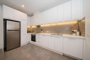 a kitchen with white cabinets and a stainless steel refrigerator at Apartment Living on the Beach in Rosebud +20 photos