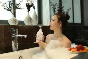a woman sitting in a bath tub holding a bottle of soap at Sea Villa FLC Sầm Sơn - Villa SB-NT in Sầm Sơn