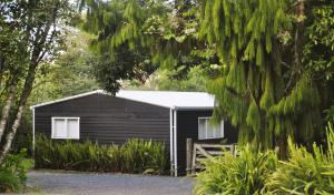 a black shed with a white roof in a forest at Lakeside Cottage with Jetty at Lake Tarawera in Rotorua