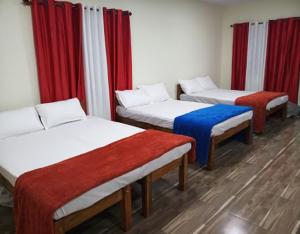 drie bedden in een kamer met rode gordijnen bij Hasiru Farms Homestay by StayApart in Mudigere