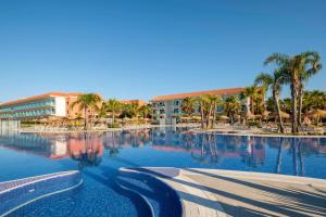 une grande piscine bordée de palmiers et un hôtel dans l'établissement Hotel Best Costa Ballena, à Costa Ballena