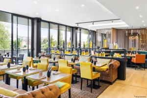 Aiden by Best Western T'aim Hotel في كومبيان: مطعم فيه كراسي صفراء وطاولات ونوافذ