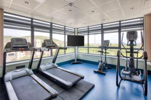 a gym with three cardio machines in a room with windows at Hôtel Aiden by Best Western Clermont-Ferrand - Le Magnetic in Clermont-Ferrand