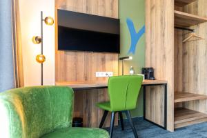 Habitación con escritorio, TV y silla verde. en Aiden by Best Western Stadtgut Hotel Steyr - FREE PARKING en Steyr
