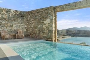 a swimming pool with two chairs and a stone wall at Radisson Blu Euphoria Resort, Mykonos in Kalo Livadi