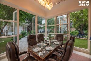 een eetkamer met een tafel, stoelen en ramen bij StayVista's Indraj Manor - Roman-Inspired Villa with Posh Interiors, Mesmerizing Garden & Outdoor Fireplace in New Delhi