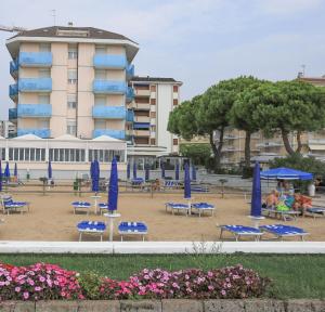 una spiaggia con sedie blu e ombrelloni di fronte a un edificio di Hotel La Bussola a Lido di Jesolo