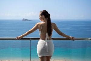 a woman in a white bikini standing in front of the ocean at Hotel Poseidon Playa in Benidorm