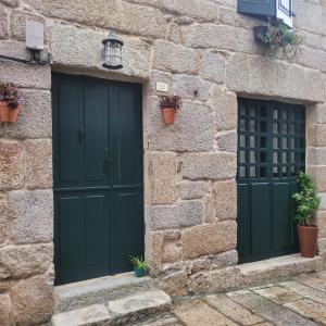 two green doors in a stone building with potted plants at El Abuelo Angel in Ribadavia