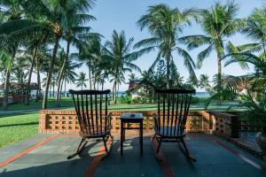 2 Stühle und ein Tisch auf einer Terrasse mit Palmen in der Unterkunft Palm Garden Beach Resort & Spa in Hoi An