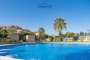een groot blauw zwembad met palmbomen en gebouwen bij Vivienda Magallanes in Sanlúcar de Barrameda