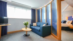 een woonkamer met een blauwe bank en een bed bij Bolton Stadium Hotel in Bolton