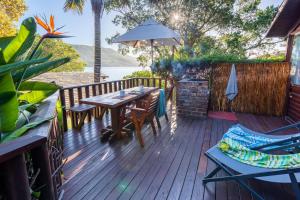 eine Holzterrasse mit einem Tisch, Stühlen und einem Sonnenschirm in der Unterkunft Under Milkwood Resort in Knysna