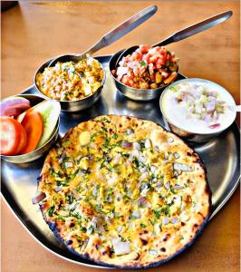 a pizza sitting on a tray with bowls of food at Hotel namo in Alwar