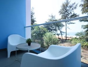 a balcony with white chairs and a table and a large window at Island Private Beach Retreat - Gokarna in Haldipur