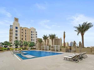a swimming pool with chairs and palm trees and buildings at StoneTree - Elegant 1 BR in Madinat Jumeirah Living Rahaal 2 in Dubai