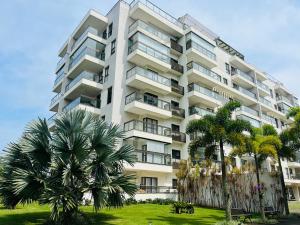 een hoog wit gebouw met palmbomen ervoor bij Apartamento Rio Marina Resort in Mangaratiba
