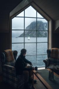 un homme assis sur une chaise devant une fenêtre dans l'établissement Reinefjorden Sjøhus, à Reine